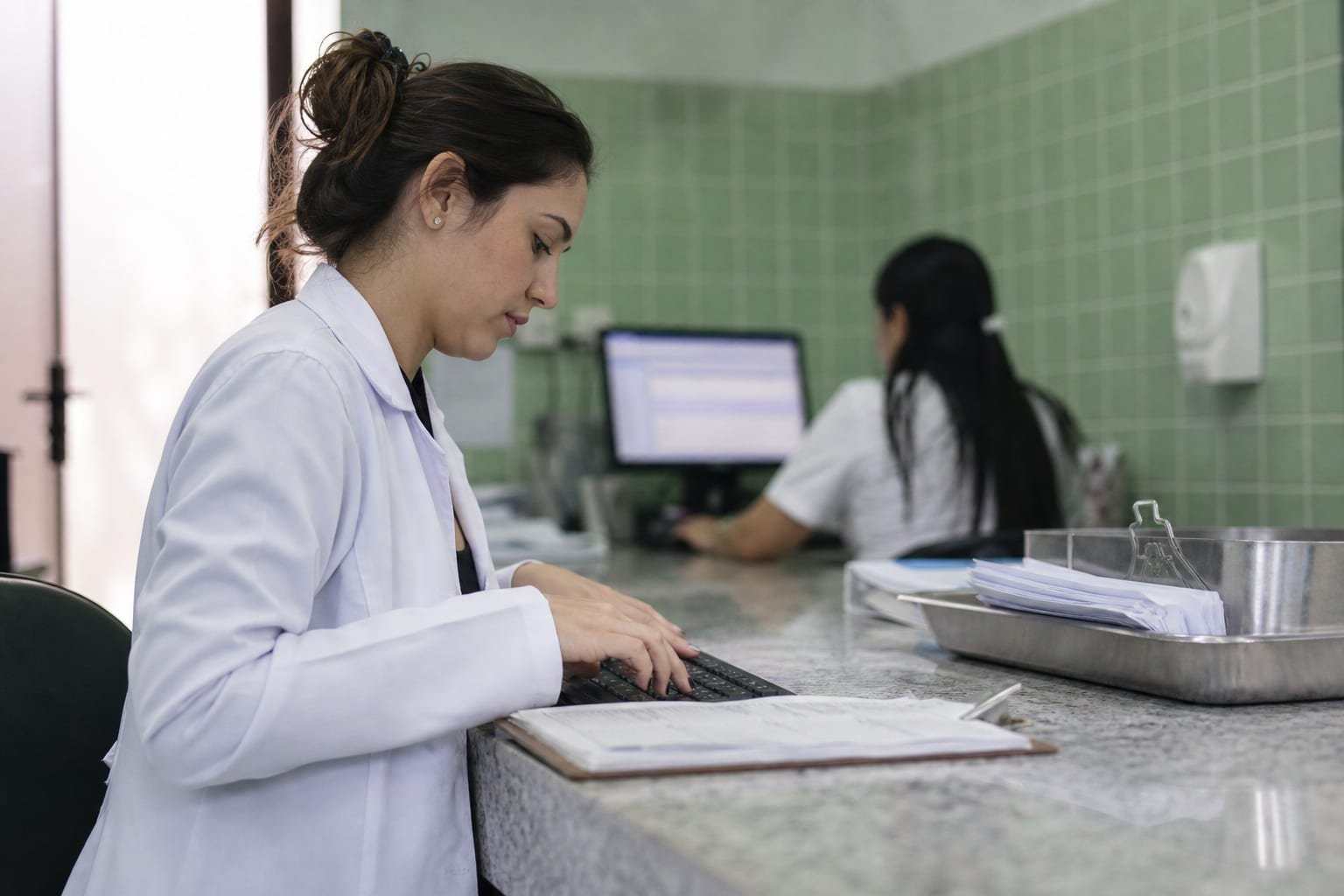 Faturista de clínica confere folhas impressas do demonstrativo enquanto digita no computador